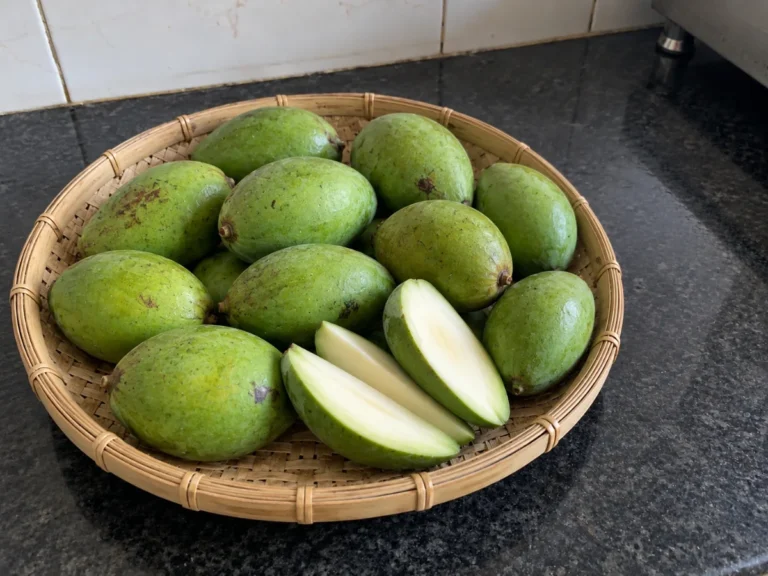 Firm, sour raw green mangoes bought in early summer for amsi achar, in a bamboo kula on a Kolkata kitchen counter
